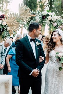 Εντυπωσιακή ξύλινη αψίδα για στολισμό δεξίωσης γάμου με αποξηραμένα φύλλα φοίνικα και μπορντό λεπτομέρειες