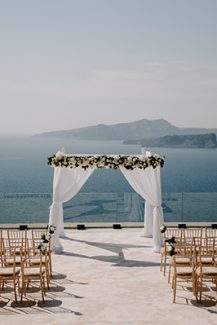 Υπέροχη αψίδα τελετής γάμου με λευκά άνθη, λευκά υφάσματα και θέα το Αιγαίο πέλαγος
