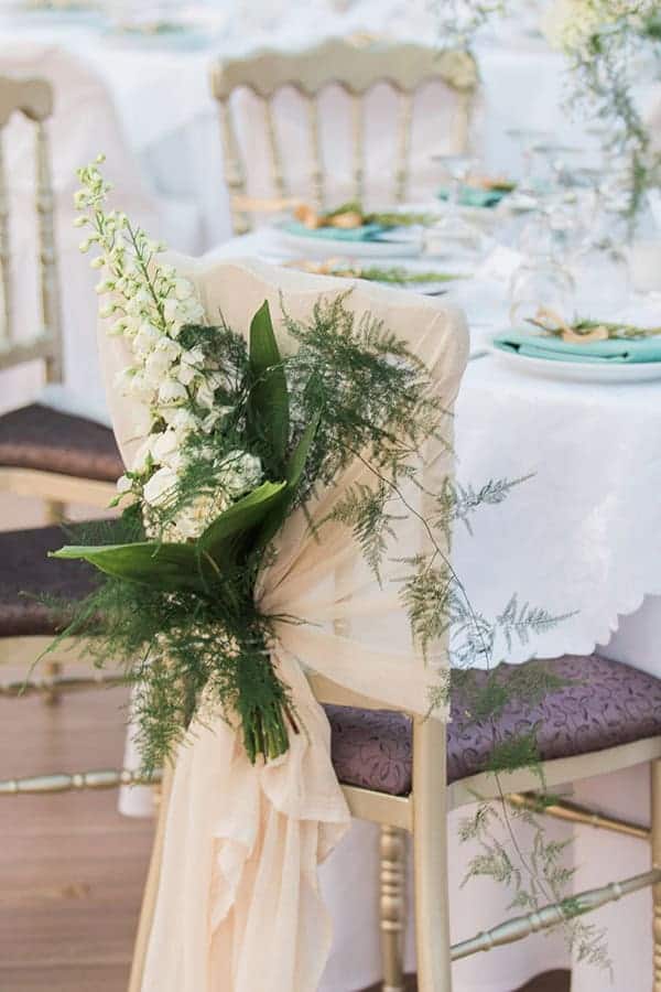Εντυπωσιακός στολισμός γαμήλιας καρέκλας με λευκά άνθη και πλούσια πρασινάδα Εντυπωσιακός στολισμός γαμήλιας καρέκλας με λευκά άνθη και πλούσια πρασινάδα