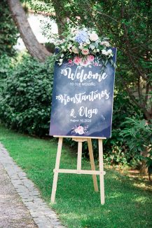 Στολισμός δεξίωσης εξωτερικού χώρου με πινακίδα καλωσορίσματος καλεσμένων σε μαύρο χρώμα