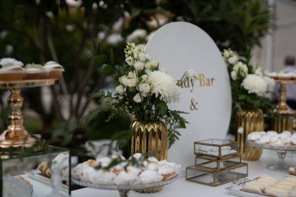 Elegant dessert table με λευκό backdrop και χρυσές βάσεις