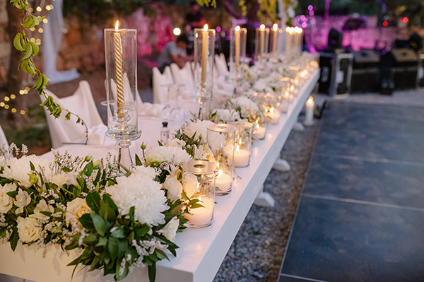 Μαγευτικός στολισμός γαμήλιου τραπεζιού με λευκά λουλούδια και ψηλά κηροπήγια