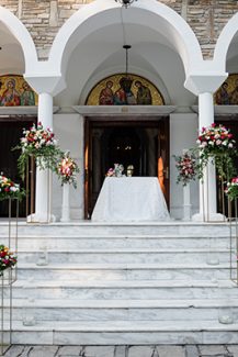 Όμορφος στολισμός εισόδου εκκλησίας με πολύχρωμα άνθη πάνω σε gold stands