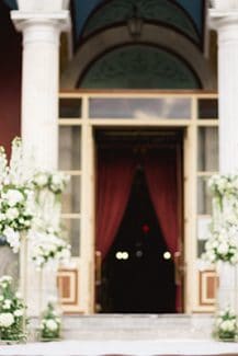 Όμορφος στολισμός εισόδου εκκλησίας με λευκά δελφίνιουμ και ορτανσίες σε gold stands